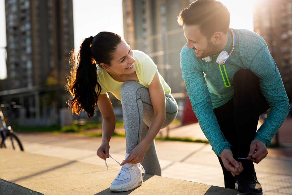 uomo e donna sconfiggono l'Inattività fisica allacciandosi le scarpe e andando a correre 