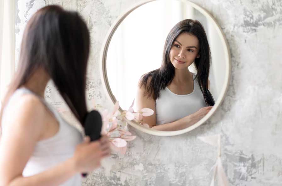 donna si cura spazzolandosi i capelli e specchiandosi