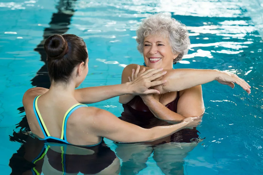 donna sorridente si allena in piscina guidata da un personal training esperto