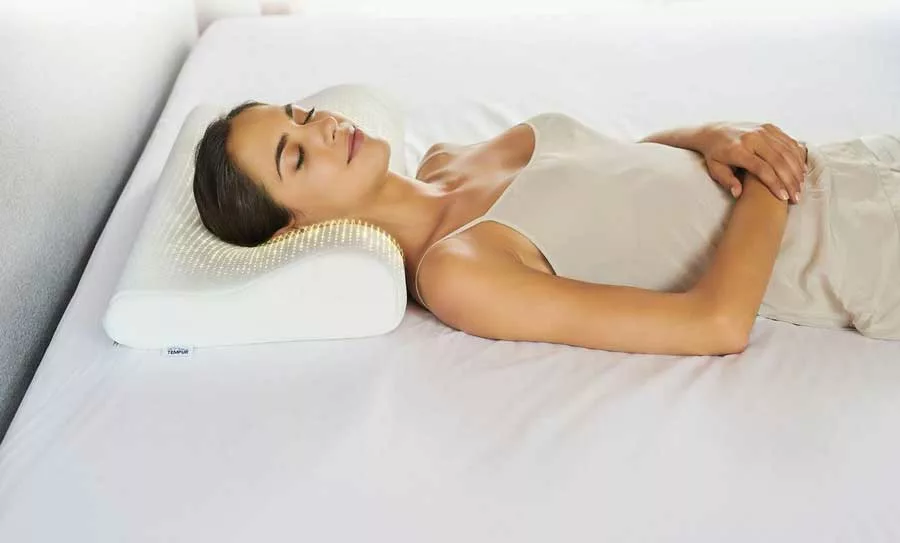 donna distesa a letto usa un cuscino specifico per il collo. Vuole evitare il torcicollo. 