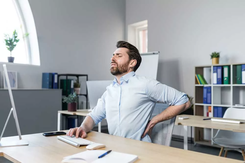 uomo che lavora in ufficio ha male alla schiena dovrebbe fare esercizi di ginnastica posturale