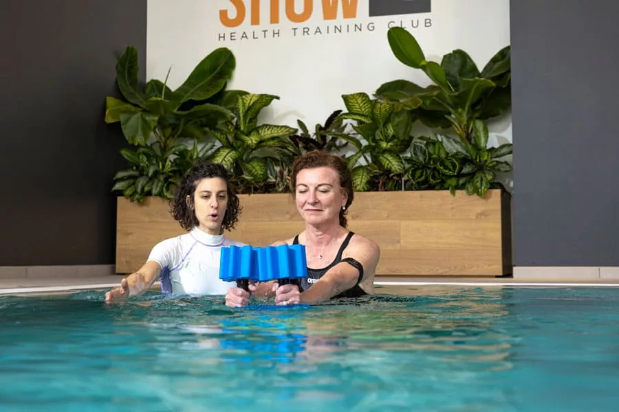 donna si allena in piscina affiancata da una personal trainer 