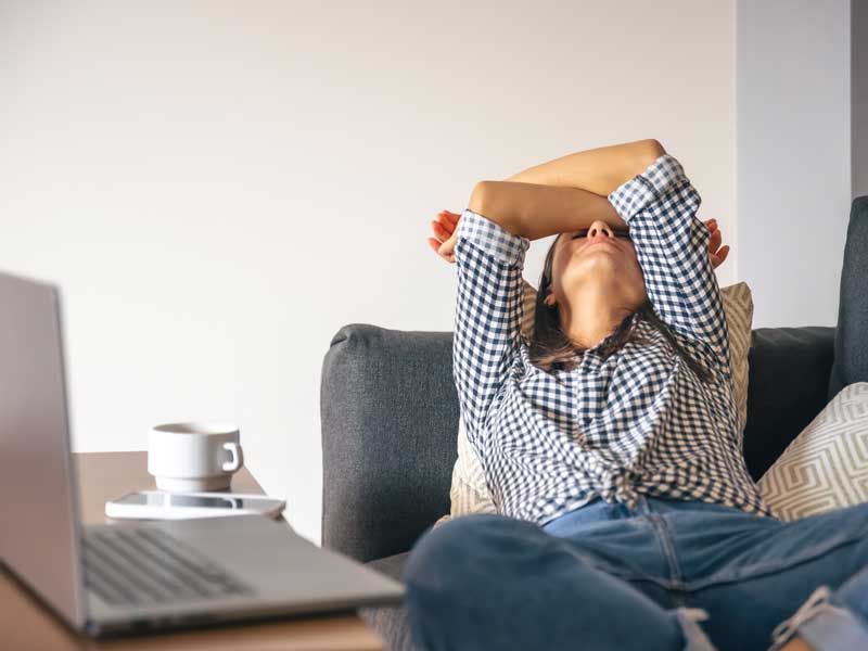 donna sedentaria sta distesa sul divano con le braccia sopra il viso