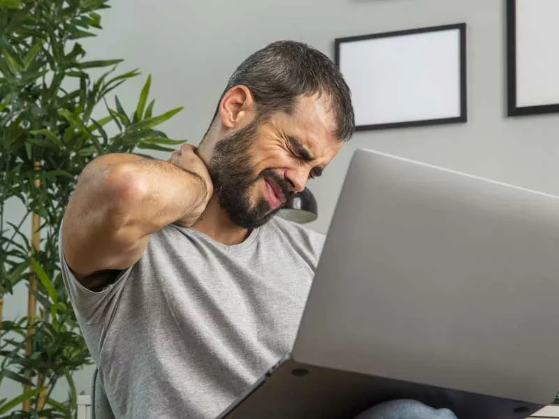 uomo è seduto in ufficio da ore ed è sedentario. Si tiene con una mano il collo perché ha male