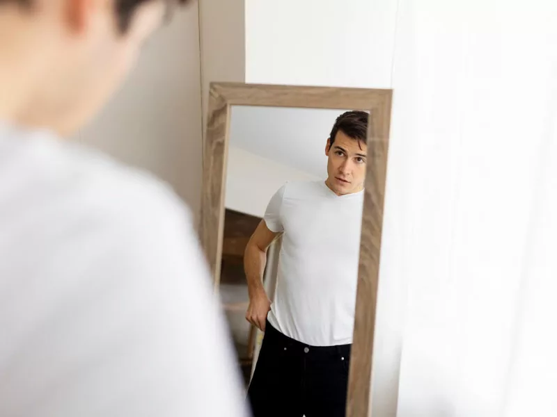 uomo si specchia-insoddisfatto perché non vede i risultati dell'allenamento