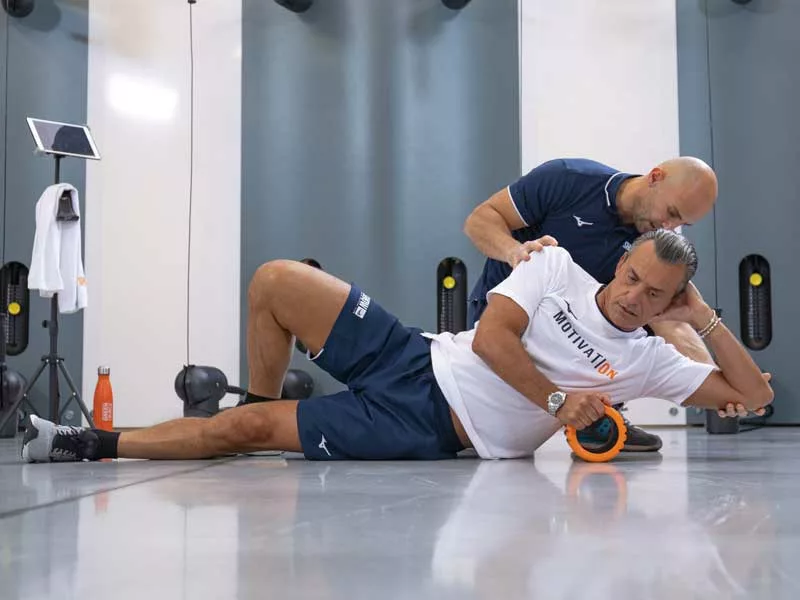 uomo fa un allenamento personalizzato con il personal trainer in palestra usando il foam roller