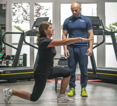 Donna esegue una croce piegata in palestra seguita da un personal trainer, durante una sessione di Training neuromotorio.