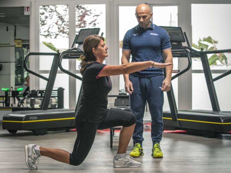 Donna esegue una croce piegata in palestra seguita da un personal trainer, durante una sessione di Training neuromotorio.