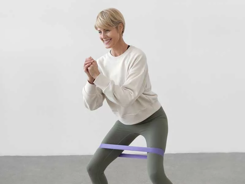 donna sorridente si allena a casa con un elastico senza fare faica