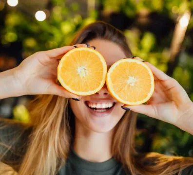 donna sorridente e felice di copre il viso con delle arance tagliate che sono degli alimenti ricchi di vitamina c