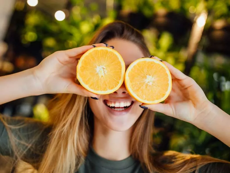 donna sorridente e felice di copre il viso con delle arance tagliate che sono degli alimenti ricchi di vitamina c
