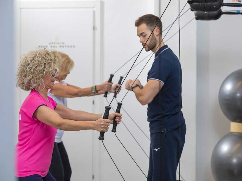 Donne svolgono un allenamento funzionale al Kinesis in palestra, seguite da un personal trainer, con focus specifico sul rinforzo della schiena.