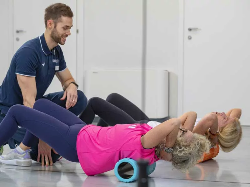 donne si allenano in palestra seguite da un personal trainer e fanno ginnastica dolce usando un foam roller