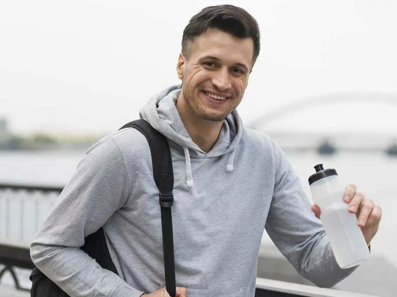 uomo sorridente beve dalla borraccia dopo il suo allenamento d'inverno