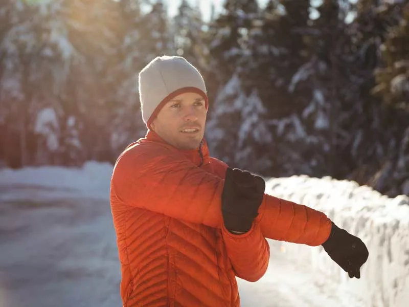 uomo bello e sorridente in inverno da stretching prima di allenarsi