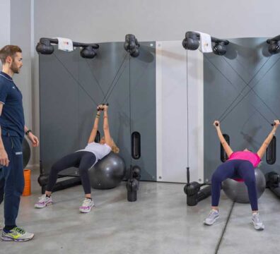 Due donne si allenano con il Kinesis in un allenamento di gruppo, seguite da un personal trainer che guida il lavoro in modo personalizzato.