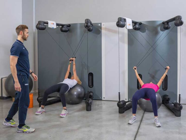 Due donne si allenano con il Kinesis in un allenamento di gruppo, seguite da un personal trainer che guida il lavoro in modo personalizzato.