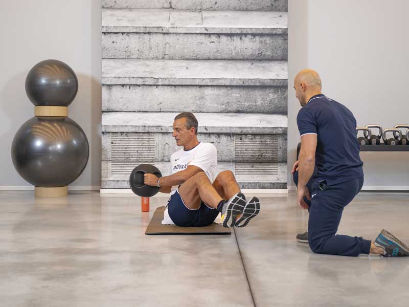 uomo allena in palestra gli addominali obliqui seguito da un personal trainer esperto
