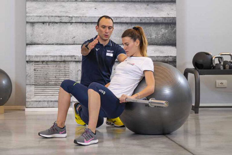 Donna si allena in palestra seguita da un personal trainer, eseguendo un allenamento funzionale con focus su addominali e dimagrimento.