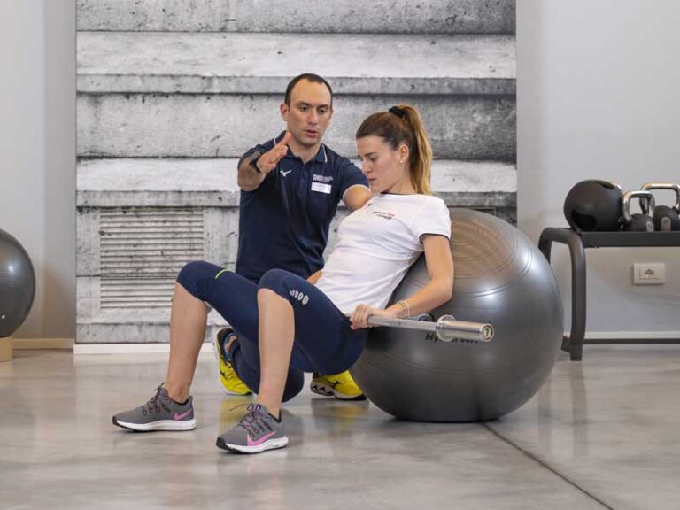 Donna si allena in palestra seguita da un personal trainer, eseguendo un allenamento funzionale con focus su addominali e dimagrimento.