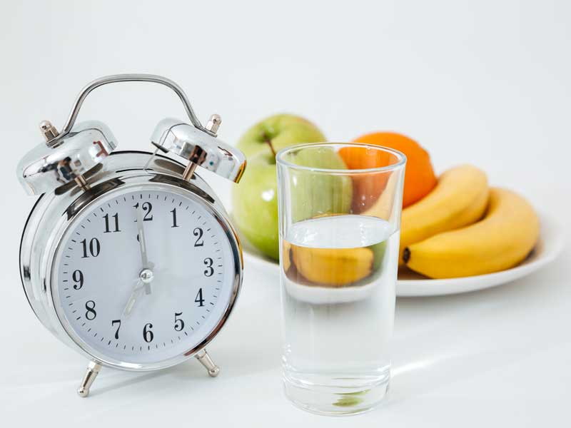sveglia, frutta e un bicchiere di acqua simbolo di digiuno