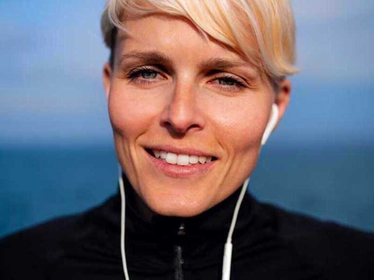 Donna in primo piano sorride, indossa abbigliamento sportivo e cuffie, pronta per fare attività fisica.