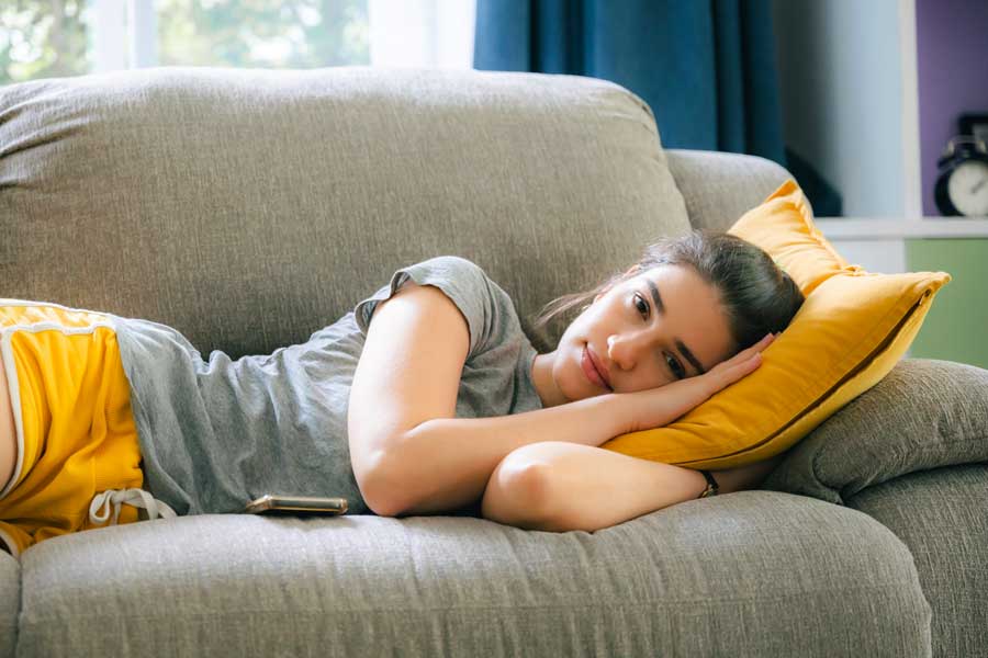 Una donna sedentaria è distesa sul divano, annoiata, con la testa appoggiata al cuscino.