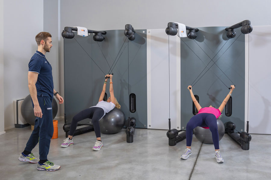 Due donne si allenano con il Kinesis in un allenamento di gruppo, seguite da un personal trainer che guida il lavoro in modo personalizzato.