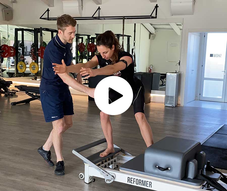 Una donna si allena con un personal trainer sul Pilates Reformer, eseguendo un esercizio mirato al dimagrimento, con l’addome contratto.