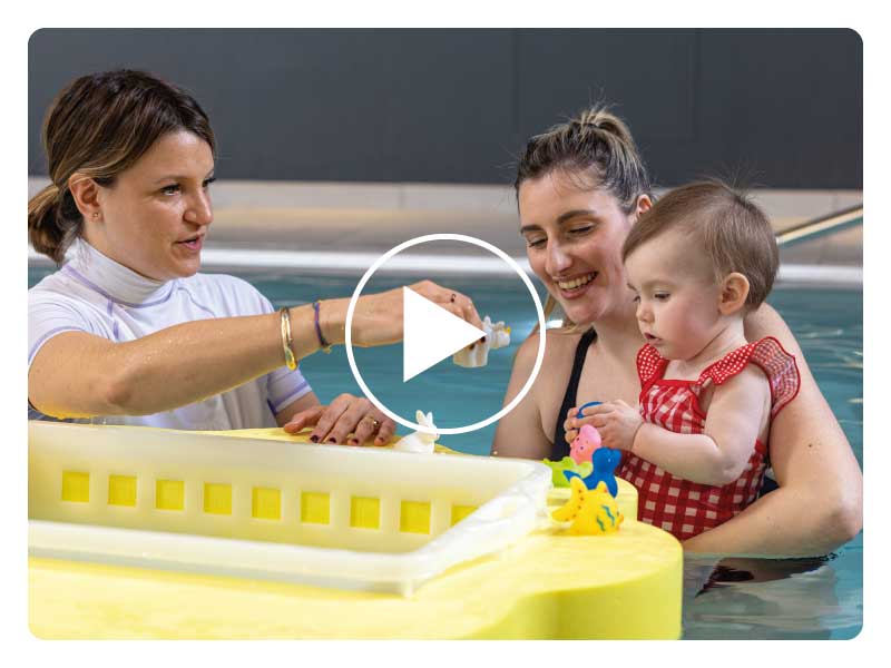 Mamma con neonato partecipa a un corso di acquaticità in piscina a Padova, seguita da un personal trainer, giocando con pupazzi galleggianti per prendere confidenza con l’acqua.