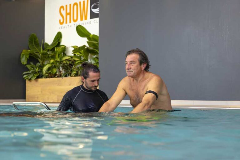 Un uomo esegue un allenamento posturale in acqua, seguito dal personal trainer che corregge la postura e guida l’esercizio.