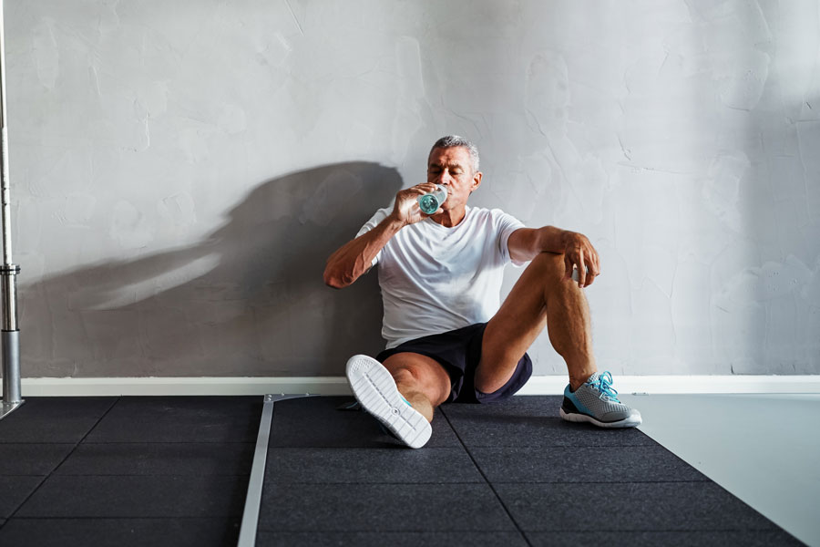 Un uomo seduto in palestra beve acqua dalla borraccia