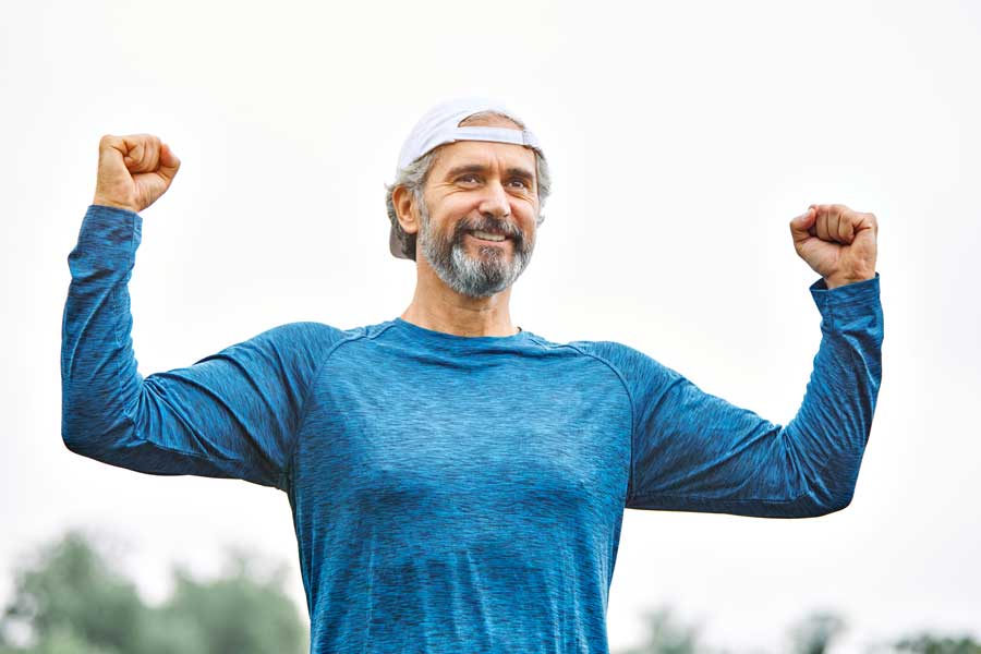 Uomo sorridente che celebra il successo del suo allenamento, con le braccia alzate.