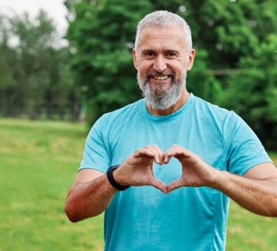 Uomo di mezza età in abbigliamento sportivo che forma un cuore con le mani, simboleggiando un allenamento benefico per il cuore.