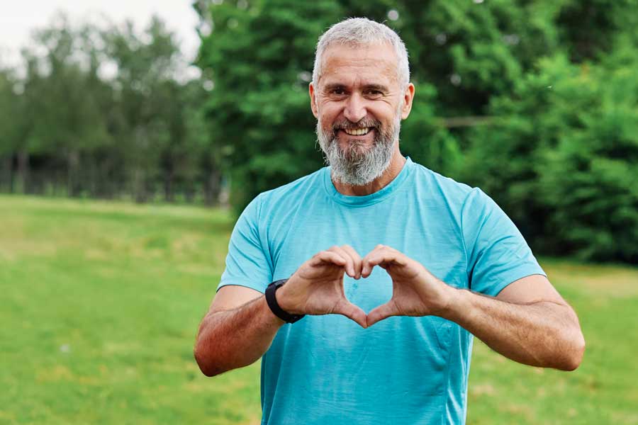 Uomo di mezza età in abbigliamento sportivo che forma un cuore con le mani, simboleggiando un allenamento benefico per il cuore.
