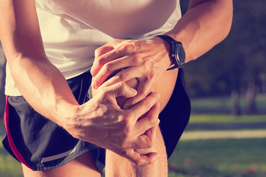 uomo si tiene il ginocchio con le mani, soffre della sindrome del corridore