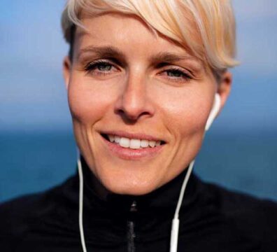 Donna in primo piano sorride, indossa abbigliamento sportivo e cuffie, pronta per fare attività fisica.