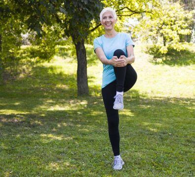 Donna si allena al parco, mantenendo l’equilibrio su una gamba sola.