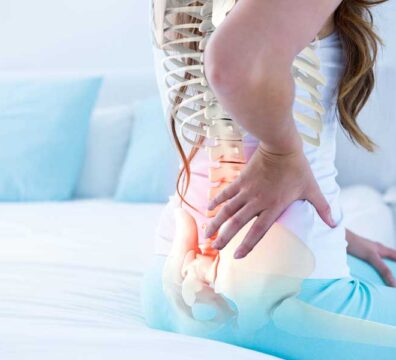Donna si sostiene la schiena con una mano a causa di un’ernia del disco.