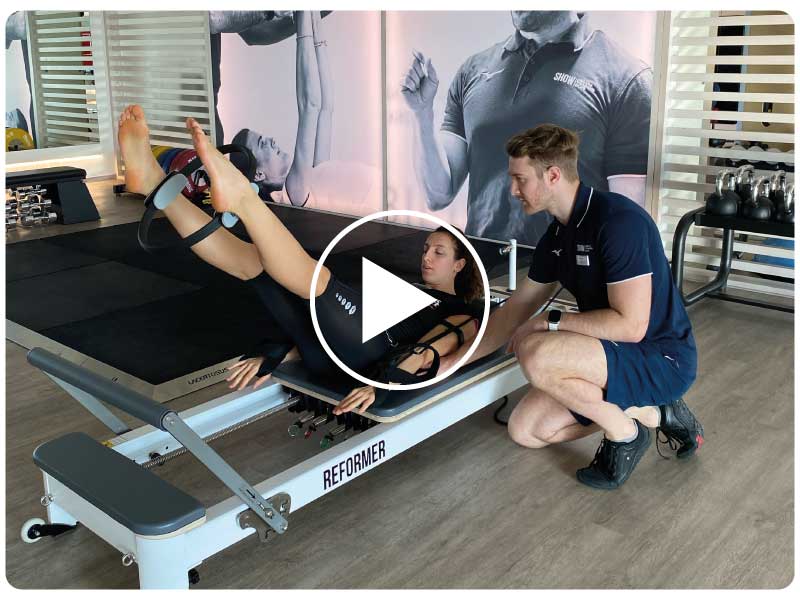 Donna esegue un allenamento di Pilates su Reformer in palestra, guidata da un personal trainer, con focus sul dimagrimento e tonificazione.