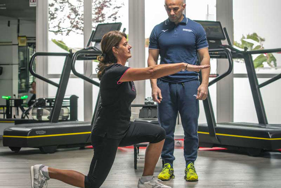 Donna esegue una croce piegata in palestra seguita da un personal trainer, durante una sessione di Training neuromotorio.