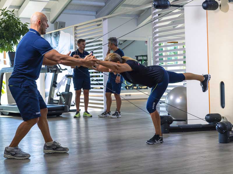 Donna in palestra che allena gli addominali e allunga la schiena con un esercizio al Kinesis, seguita dal personal trainer.
