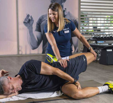Personal trainer assiste il cliente durante il riscaldamento, aiutandolo nello stretching di quadricipiti e psoas.