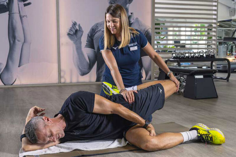 Personal trainer assiste il cliente durante il riscaldamento, aiutandolo nello stretching di quadricipiti e psoas.