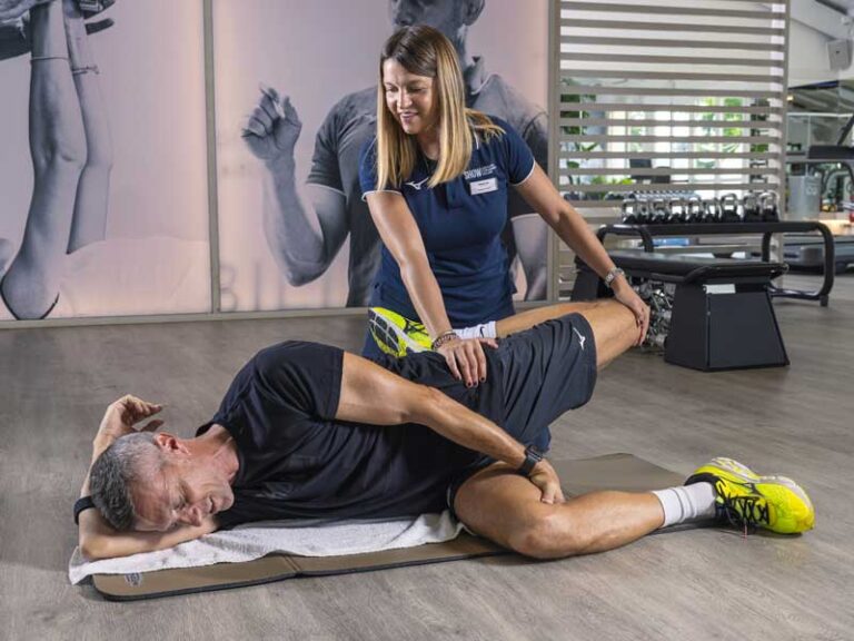 Personal trainer assiste il cliente durante il riscaldamento, aiutandolo nello stretching di quadricipiti e psoas.