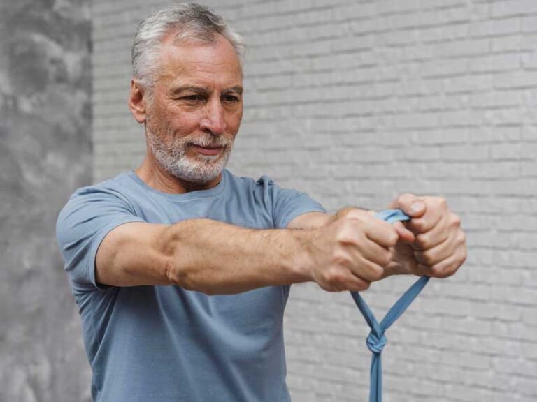 Uomo anziano vestito sportivo si allena con un elastico, esercitando la forza per prevenire cadute accidentali.