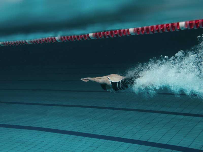 Donna immersa in piscina, appena tuffata, pronta a iniziare a nuotare.