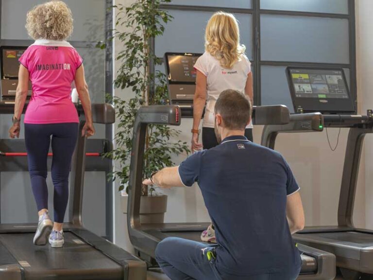 donne fanno allenamento di gruppo. Camminano sul tapis roulant gudate da un personal trainer che guarda come appoggiano i piedi