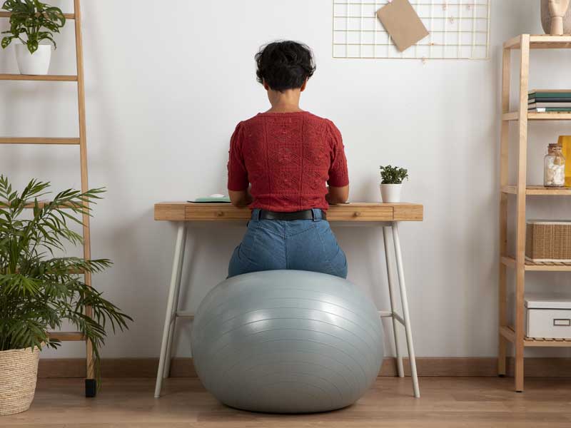 donna con postura corretta in ufficio. è seduta su una palla con la schiena dritta.