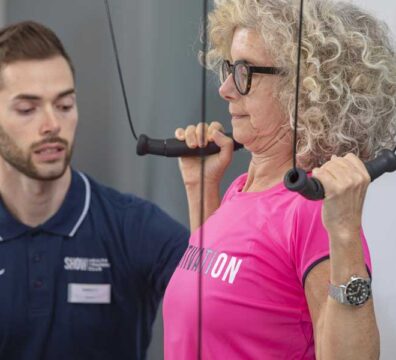 Donna in palestra esegue un allenamento di forza al Kinesis per contrastare l’artrosi, affiancata dal personal trainer che la guida.